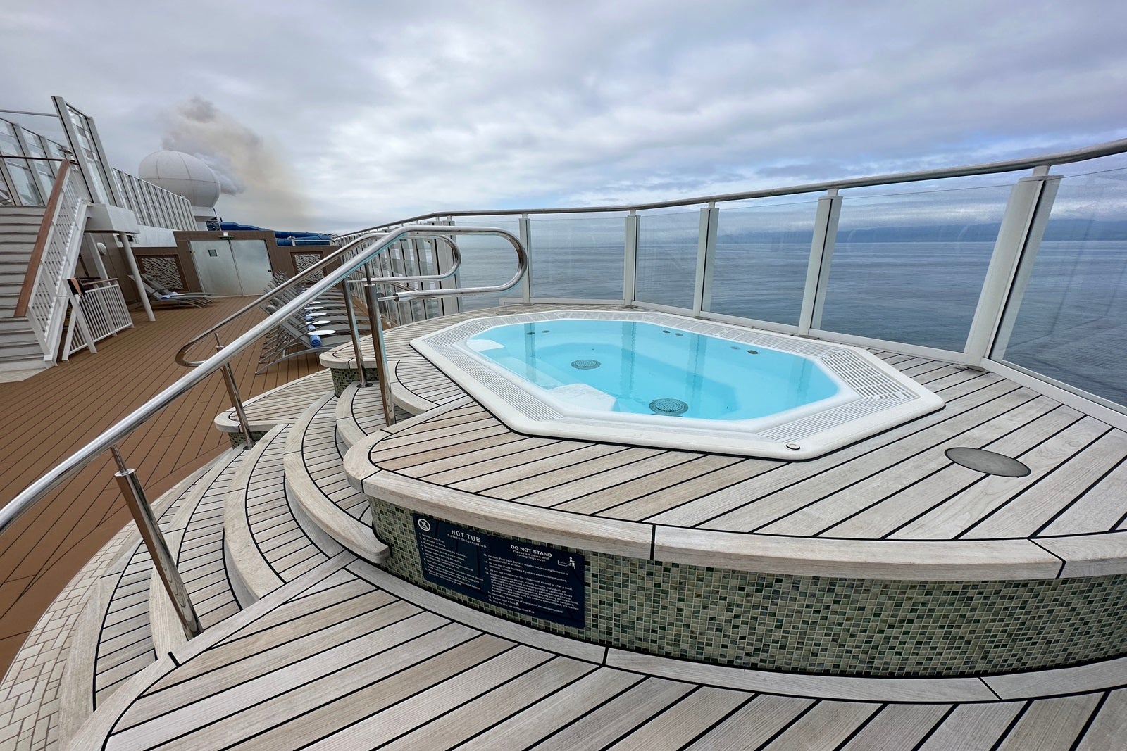 A cruise ship hot tub and railings raised on tiered decking and overlooking the ocean