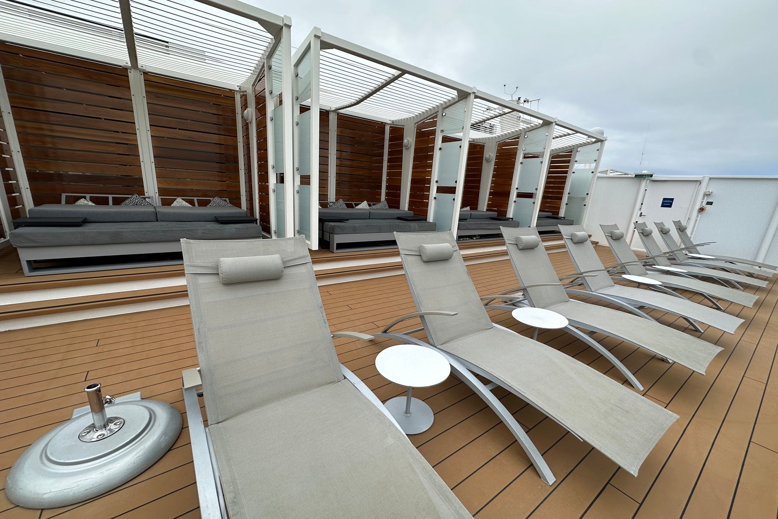 A row of deck chairs on a cruise ship sun deck in front of a row of padded cabana alcoves