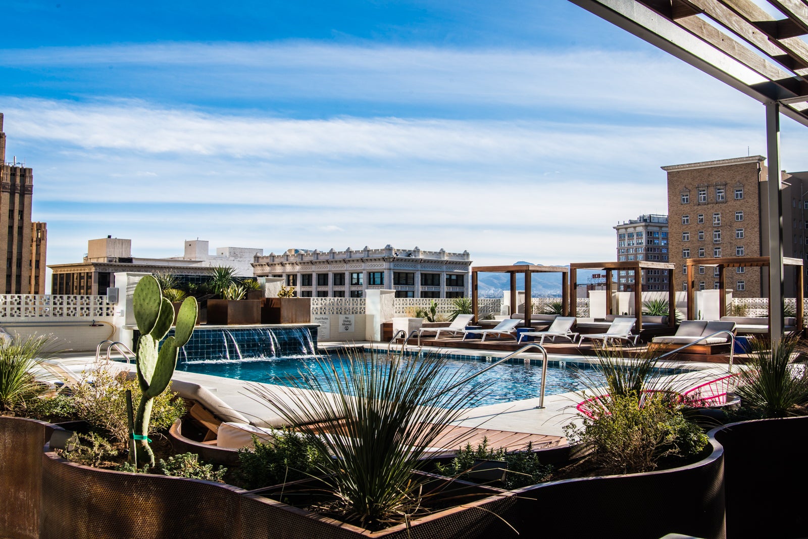 hotel rooftop pool with waterfall and cabanas overlooking city