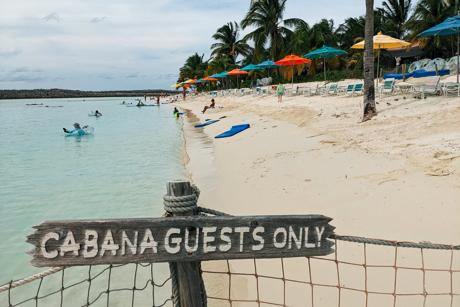 Wooden sign reading "cabana guests only" with sandy beach and palm trees behind