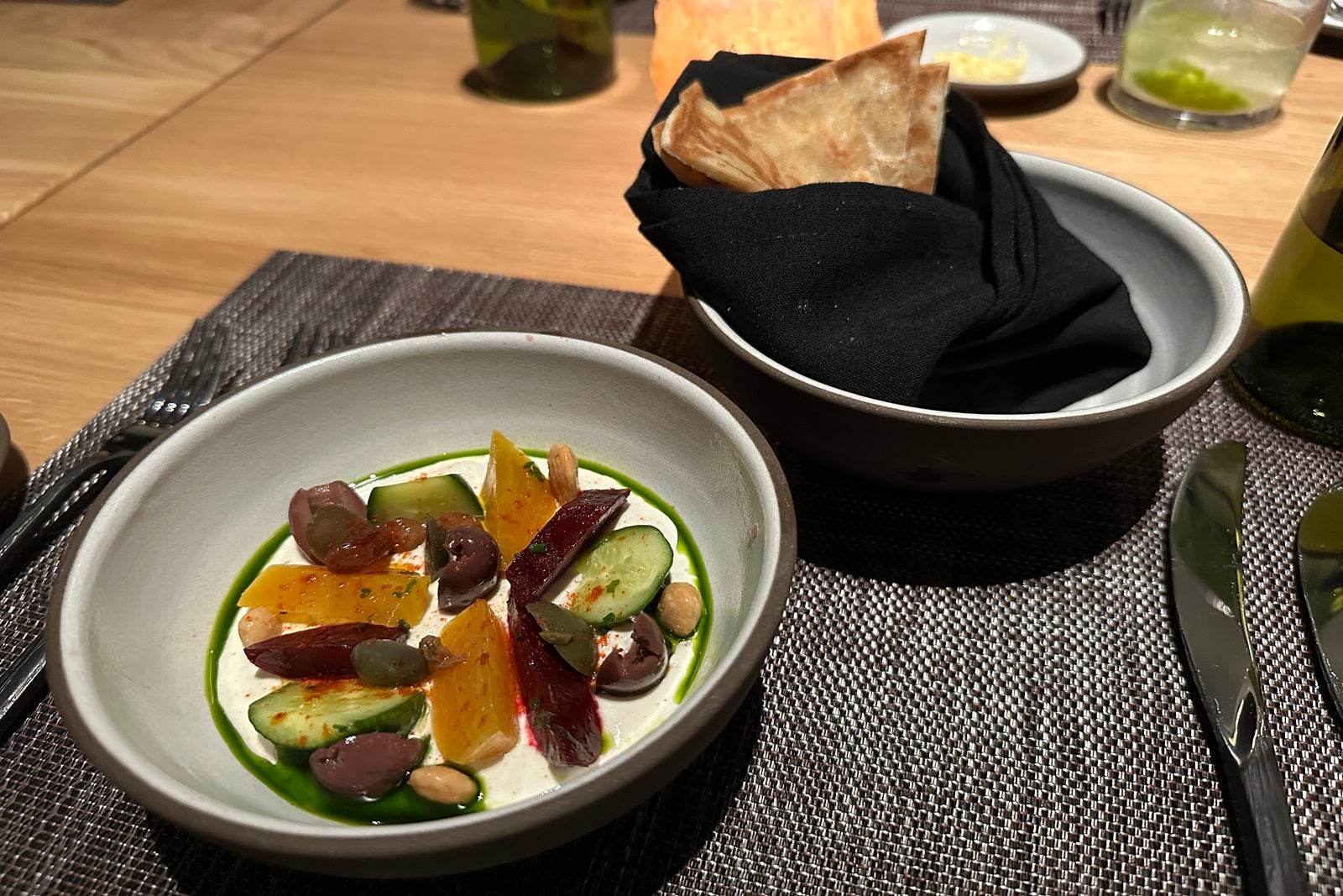 A bowl of labneh yogurt topped with beets and cucumbers with a bowl of naan bread behind it