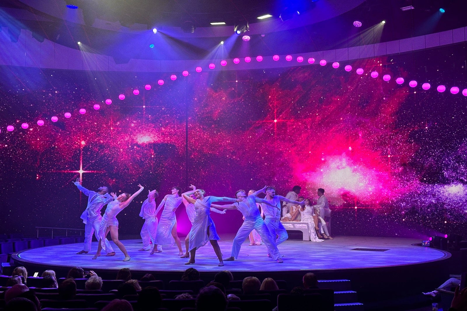 A group of singers and dancers on a stage with purple and pink LED lighting in the background