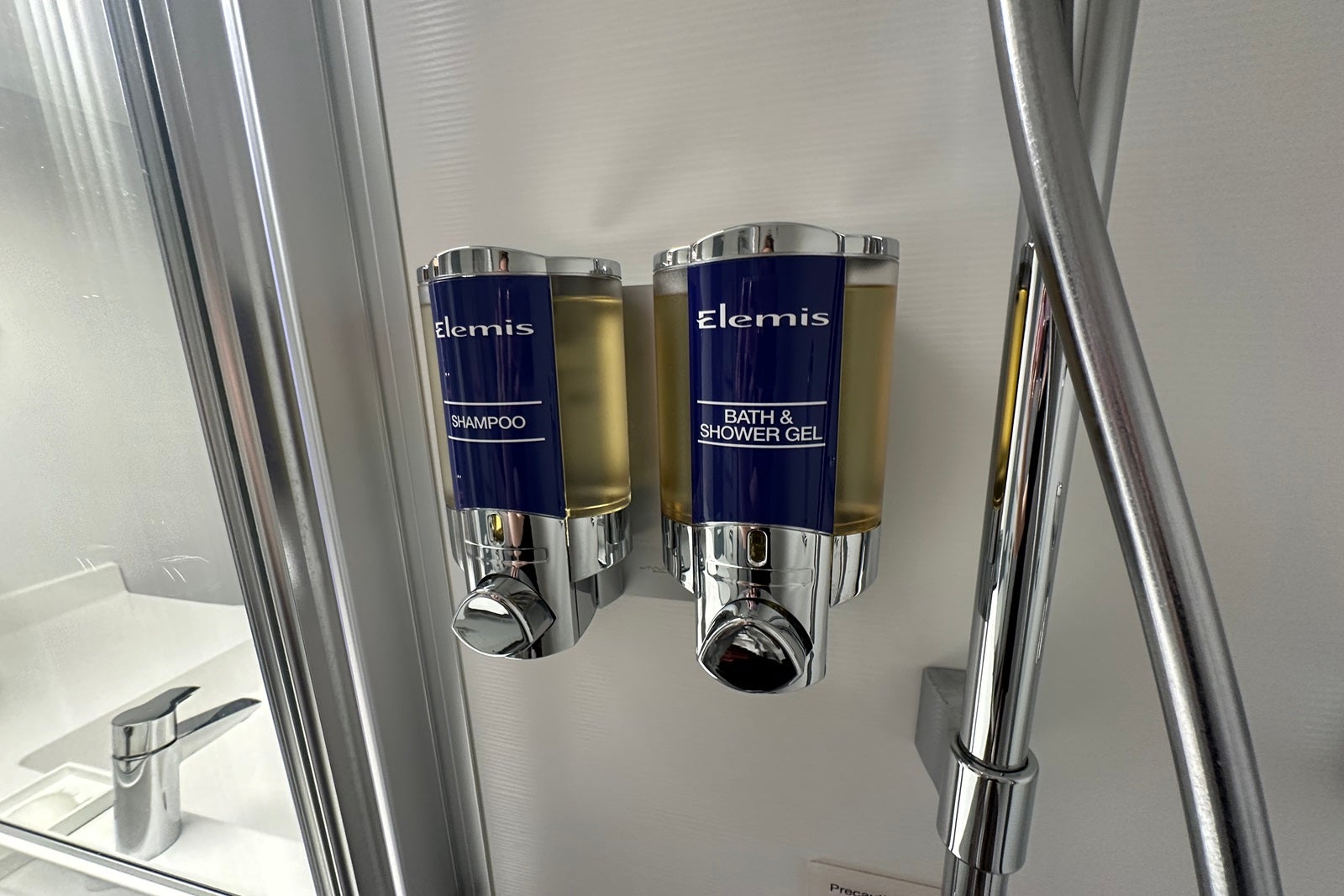 Two bottles of Elemis shower gel and shampoo hanging on the wall of a shower