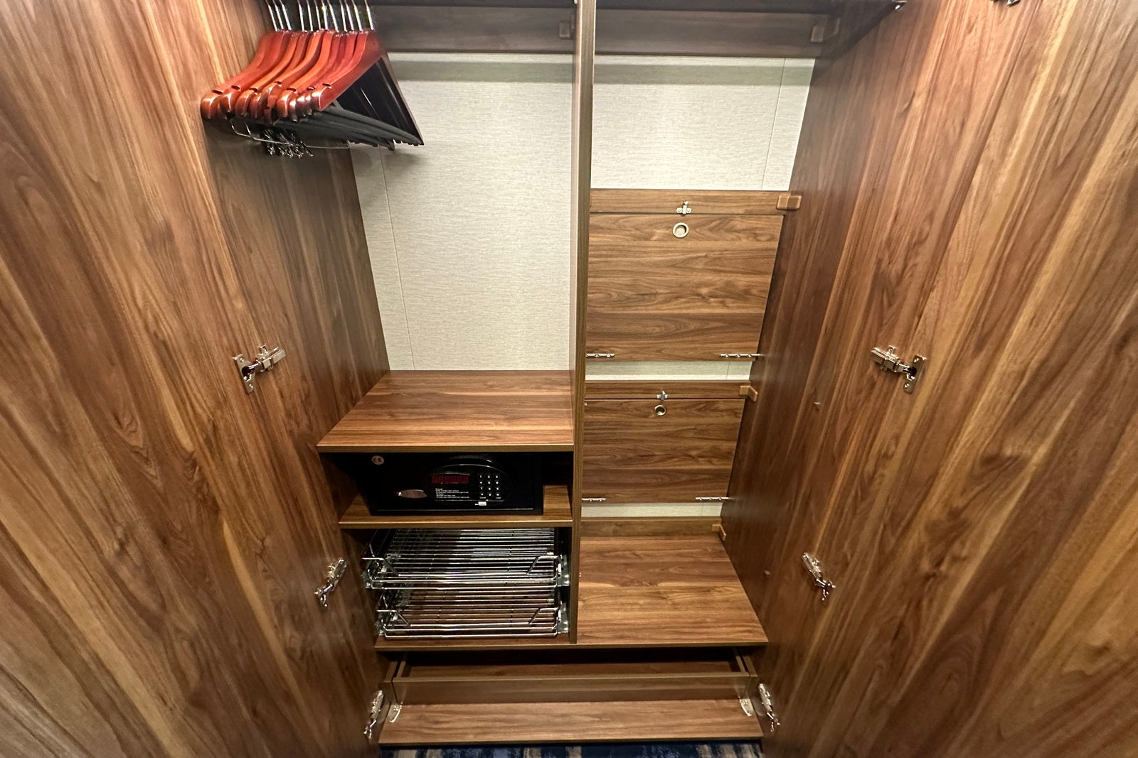 A wooden closet with wooden hangers and shelves, plus wire drawers and a safe