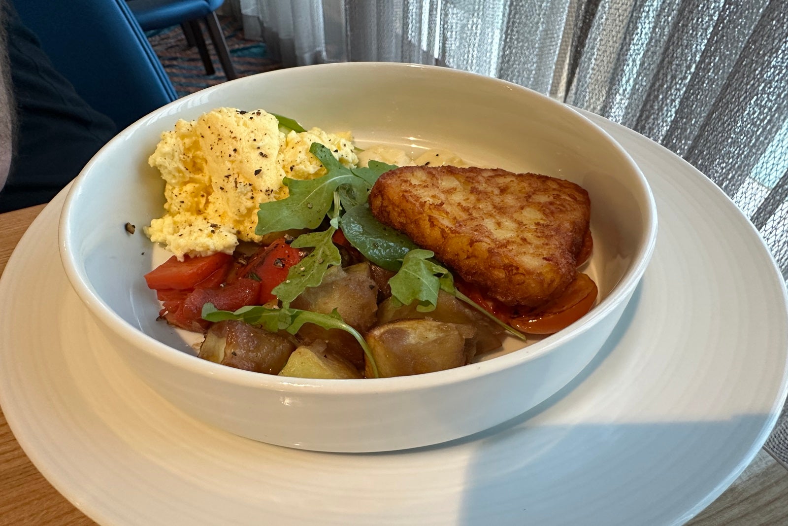 A breakfast bowl with a hashbrown in a white bowl set on a table
