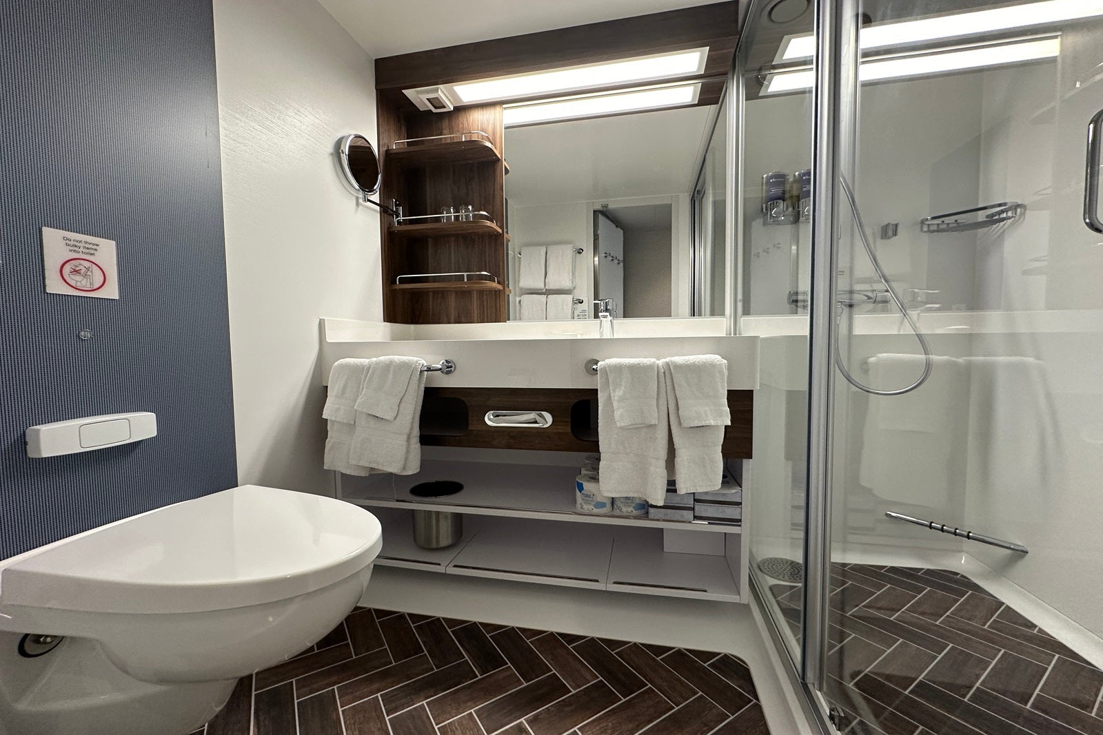 A cruise ship bathroom with a toilet, dual sink, mirror, shower and towels