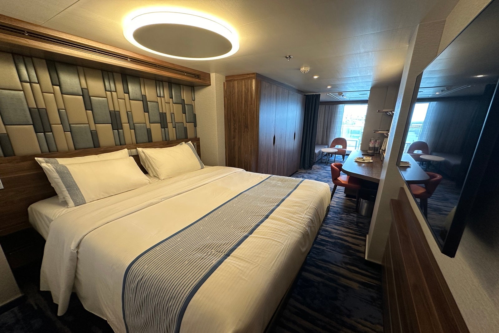 A cruise ship cabin with a queen bed a closet, a sofa, a vanity and a balcony