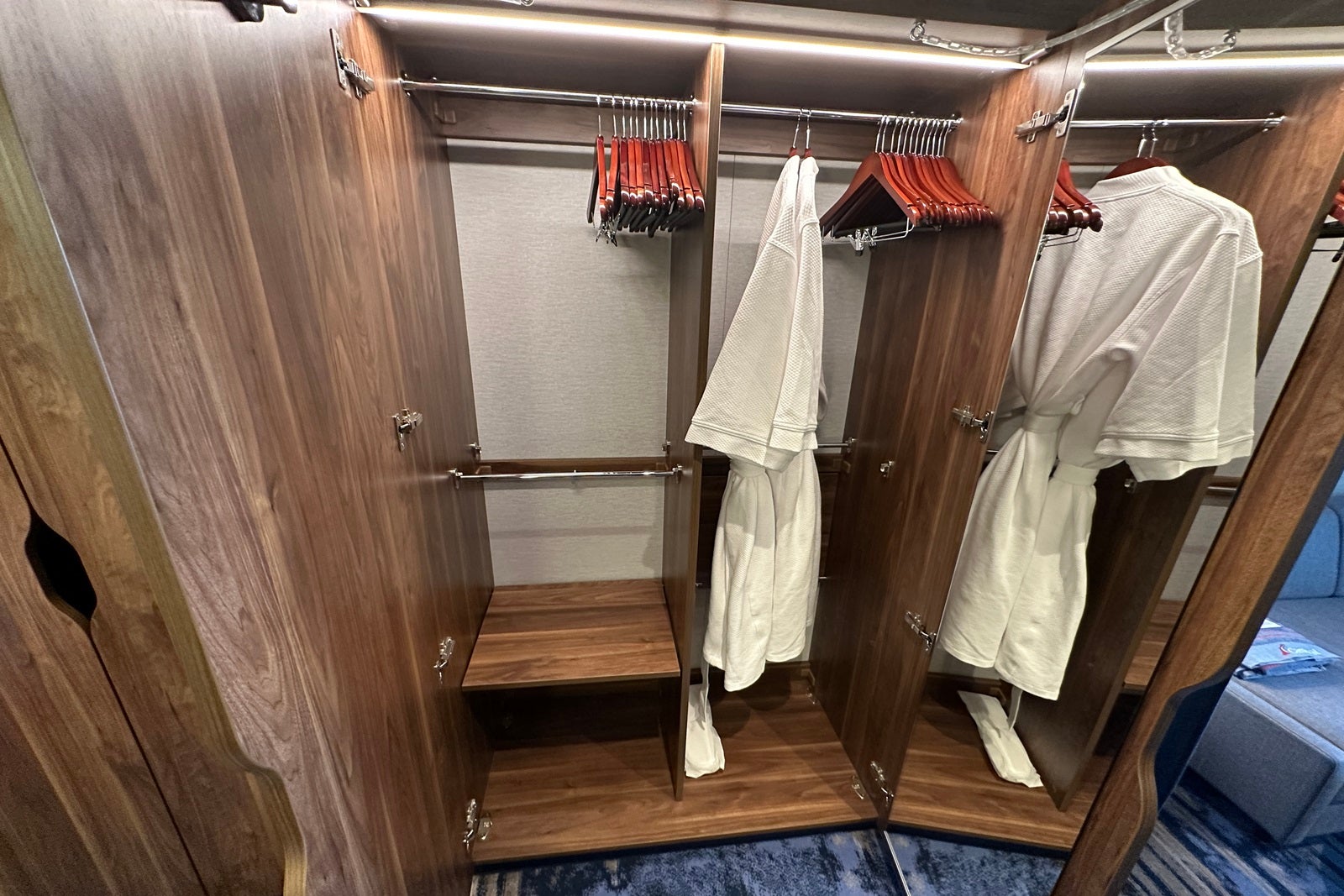 Two robes and some wooden hangers hang in a wooden closet with shelves