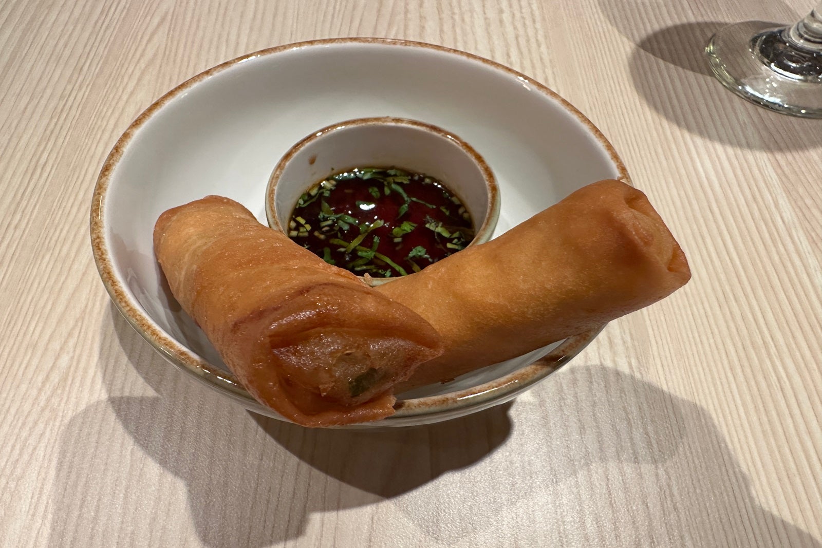 A white bowl with two spring rolls and a dish of dipping sauce
