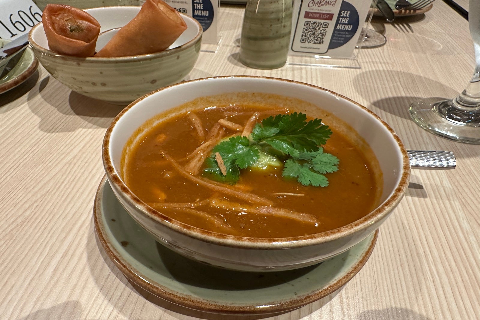 A bowl of soup with tortilla strips and a garnish in a white bowl on a table