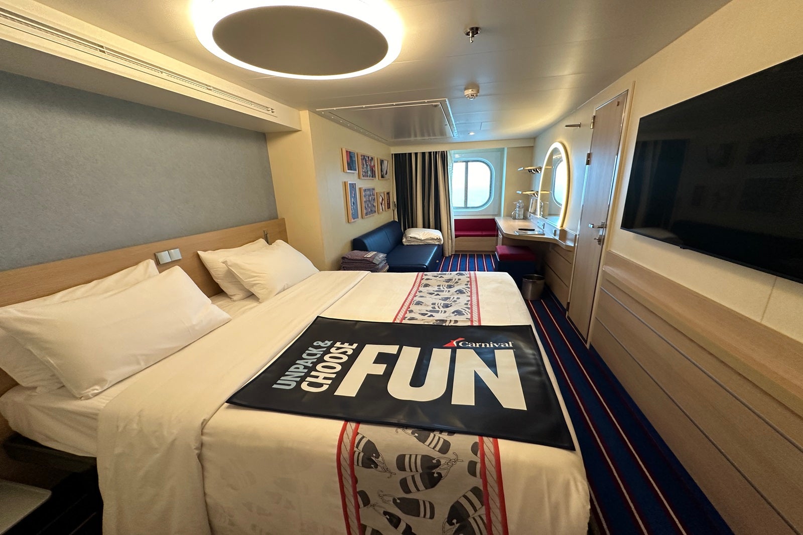 A cruise ship cabin with a queen bed and a blue and red luggage runner