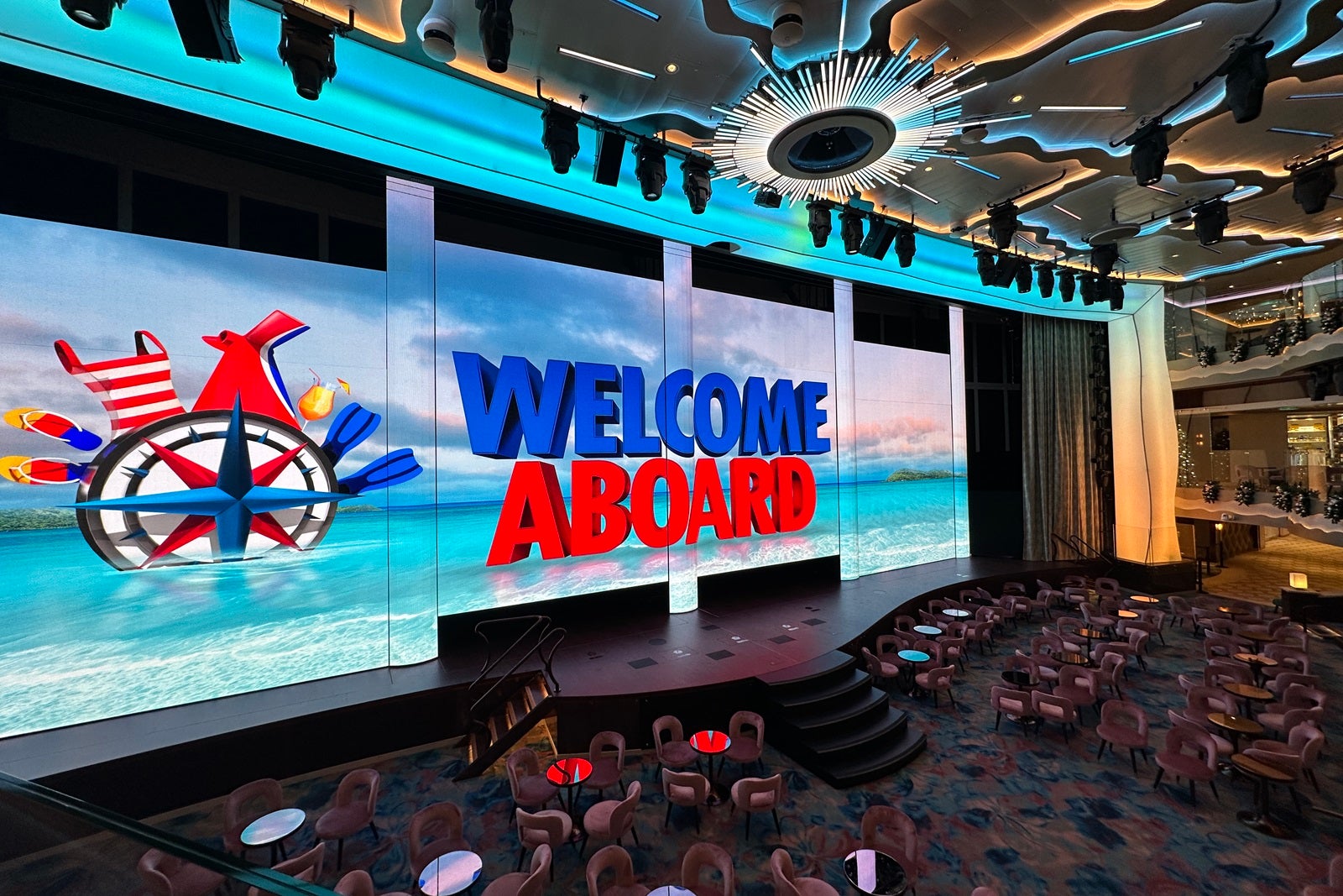 A "Welcome aboard" message appears on an LED screen in the atrium of a cruise ship