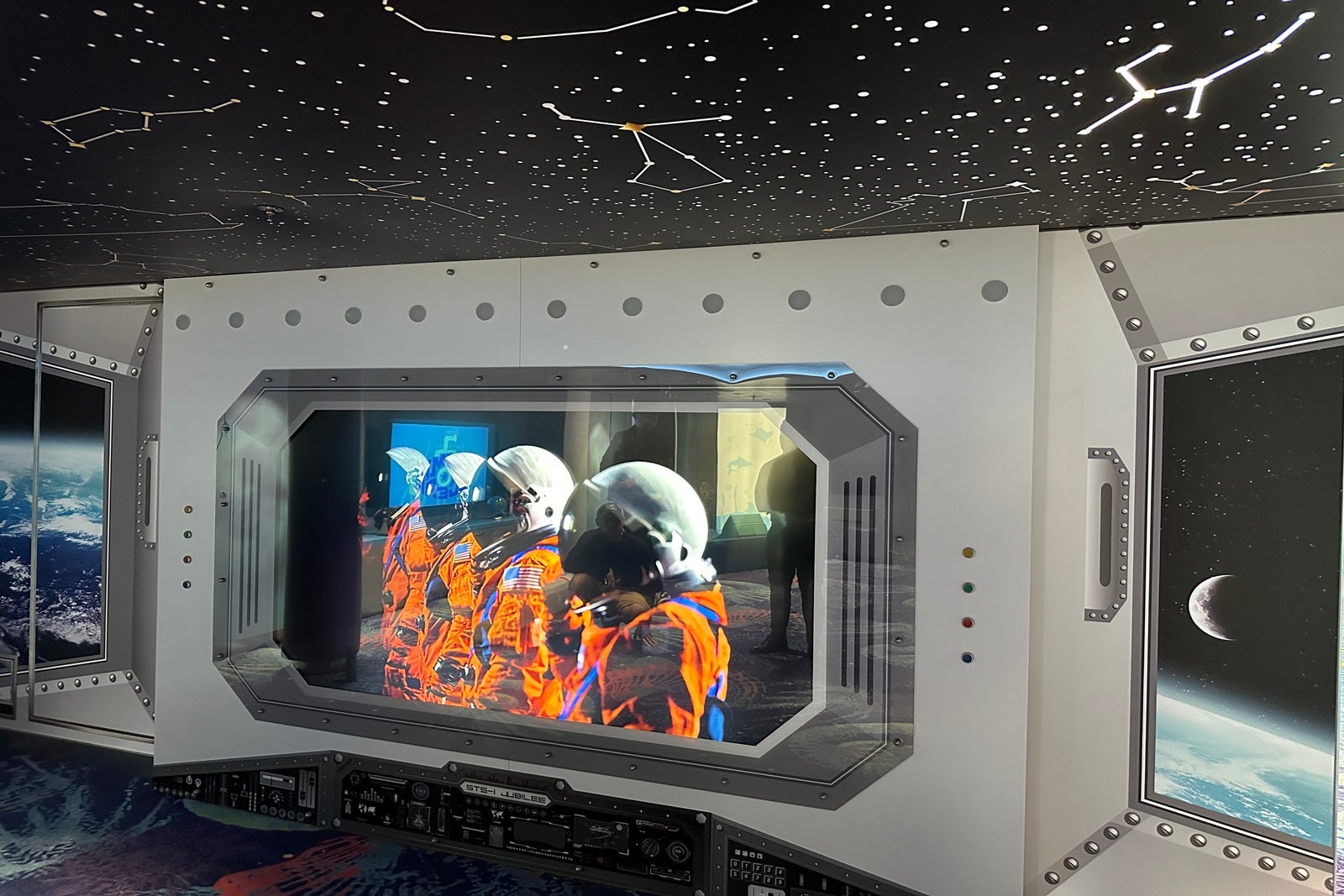 A digital display showing a team of astronauts topped with a light-up ceiling panel of the constellations