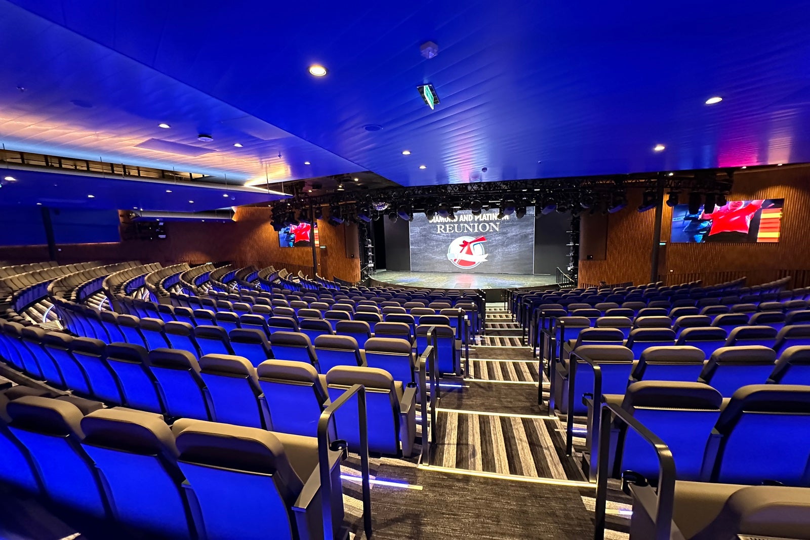 A view of a cruise ship theater from the back with the stage in front and seating all around