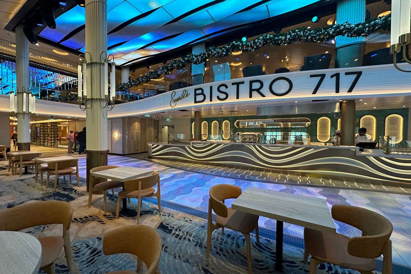 A counter-service restaurant along a cruise ship indoor promenade with seating in front