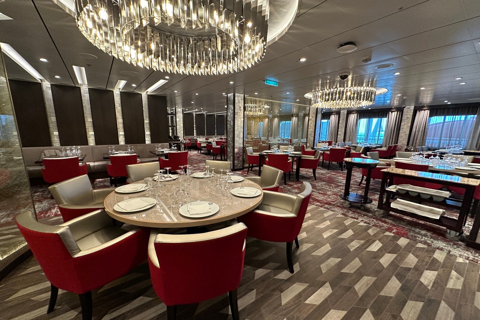 A round table set with plates surrounded by red upholstered chairs and topped with a round chandelier