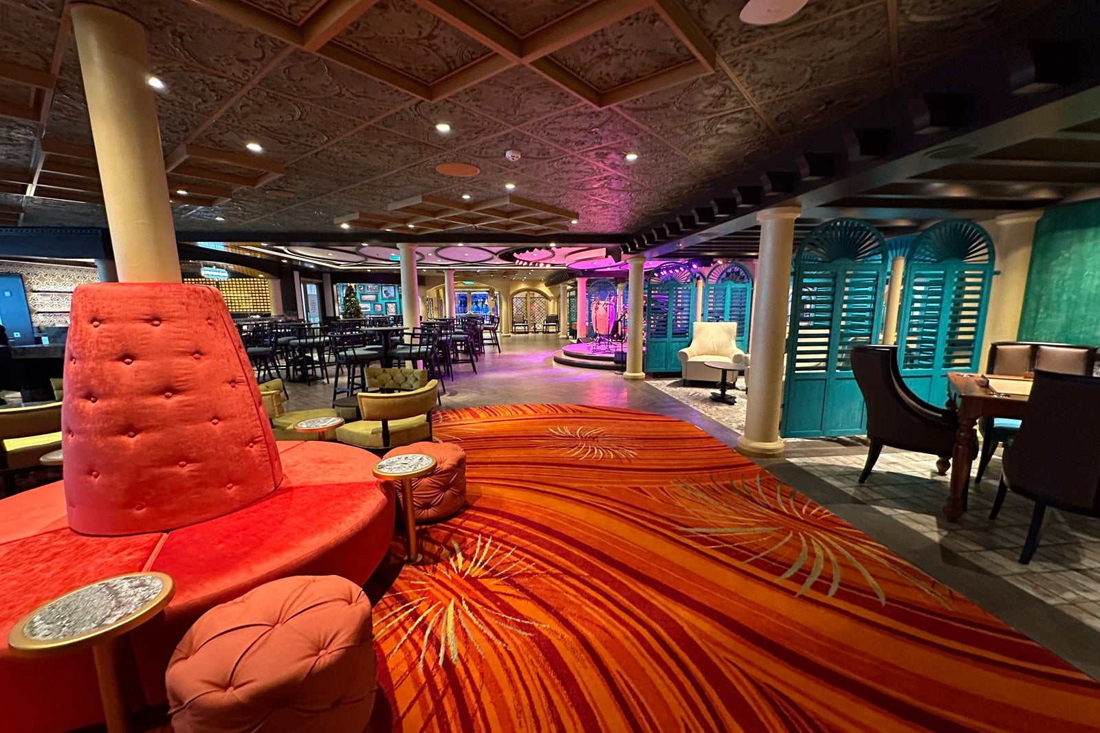 A lounge with bright orange carpet, an orange sofa and several seating alcoves in bright colors like magenta and turquoise