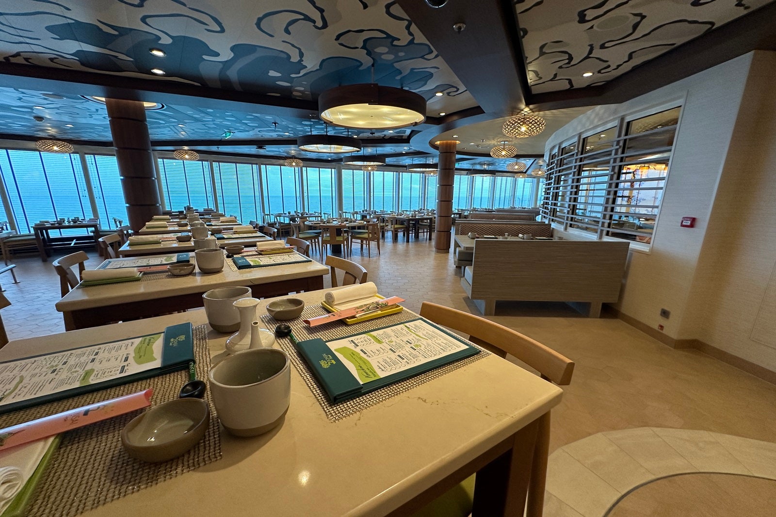 A sushi restaurant with high-top tables set with menus, chopsticks and teacups
