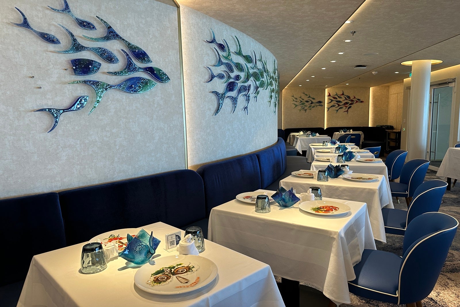 A restaurant with tables set around a curved wall that's adorned with blue glass fish
