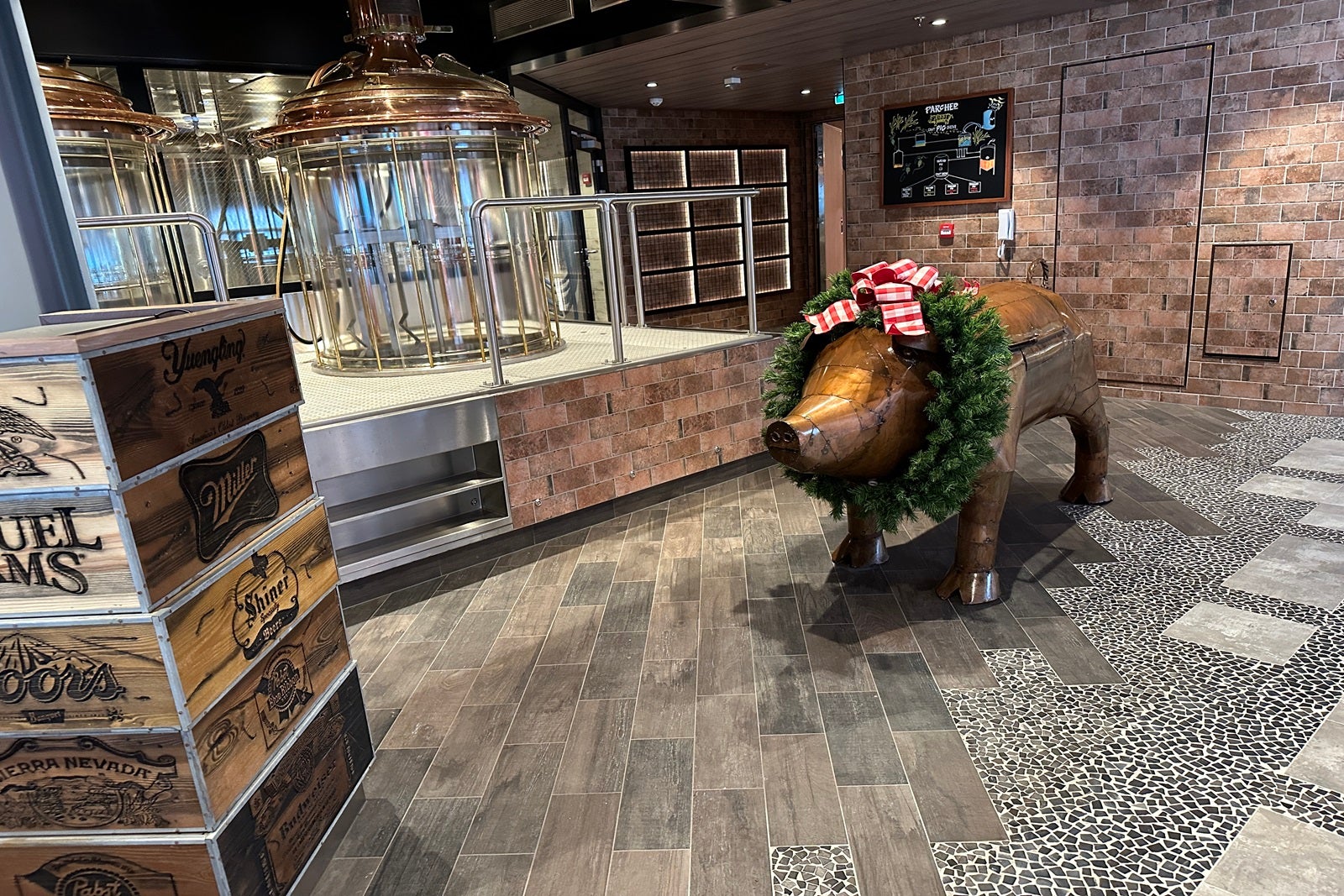 A metal pig sculpture with a holiday wreath around its neck stands near a check-in podium for a barbecue restaurant