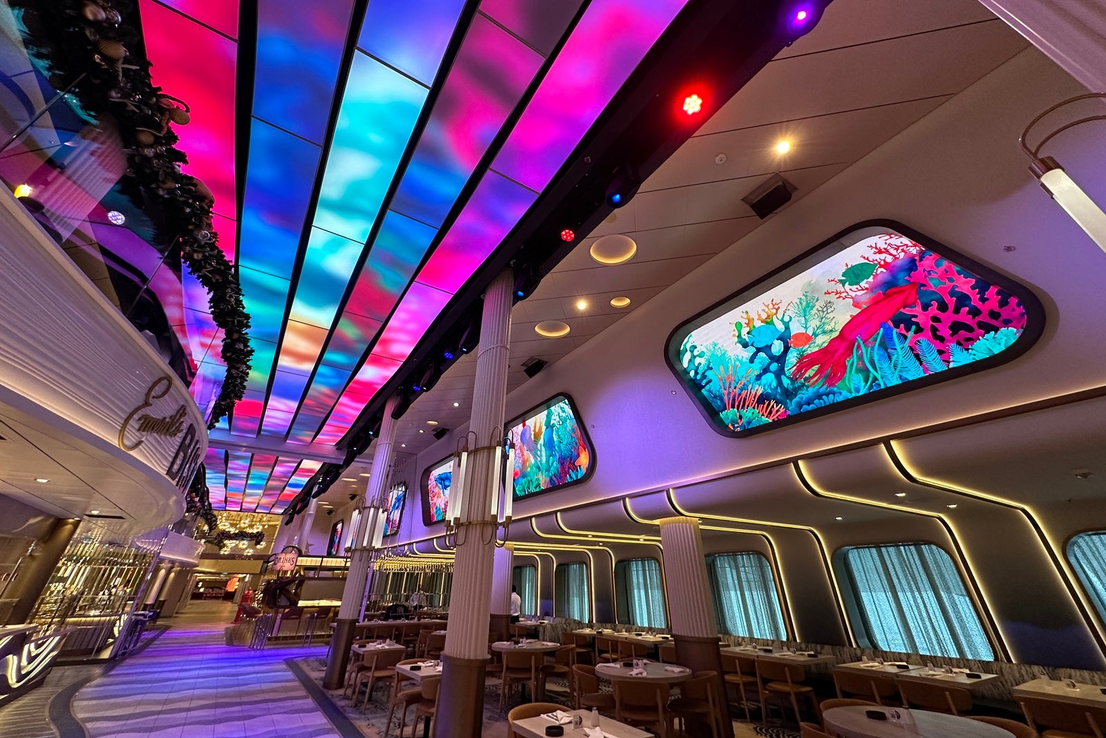 A cruise-ship indoor promenade with colorful LED screens and seating