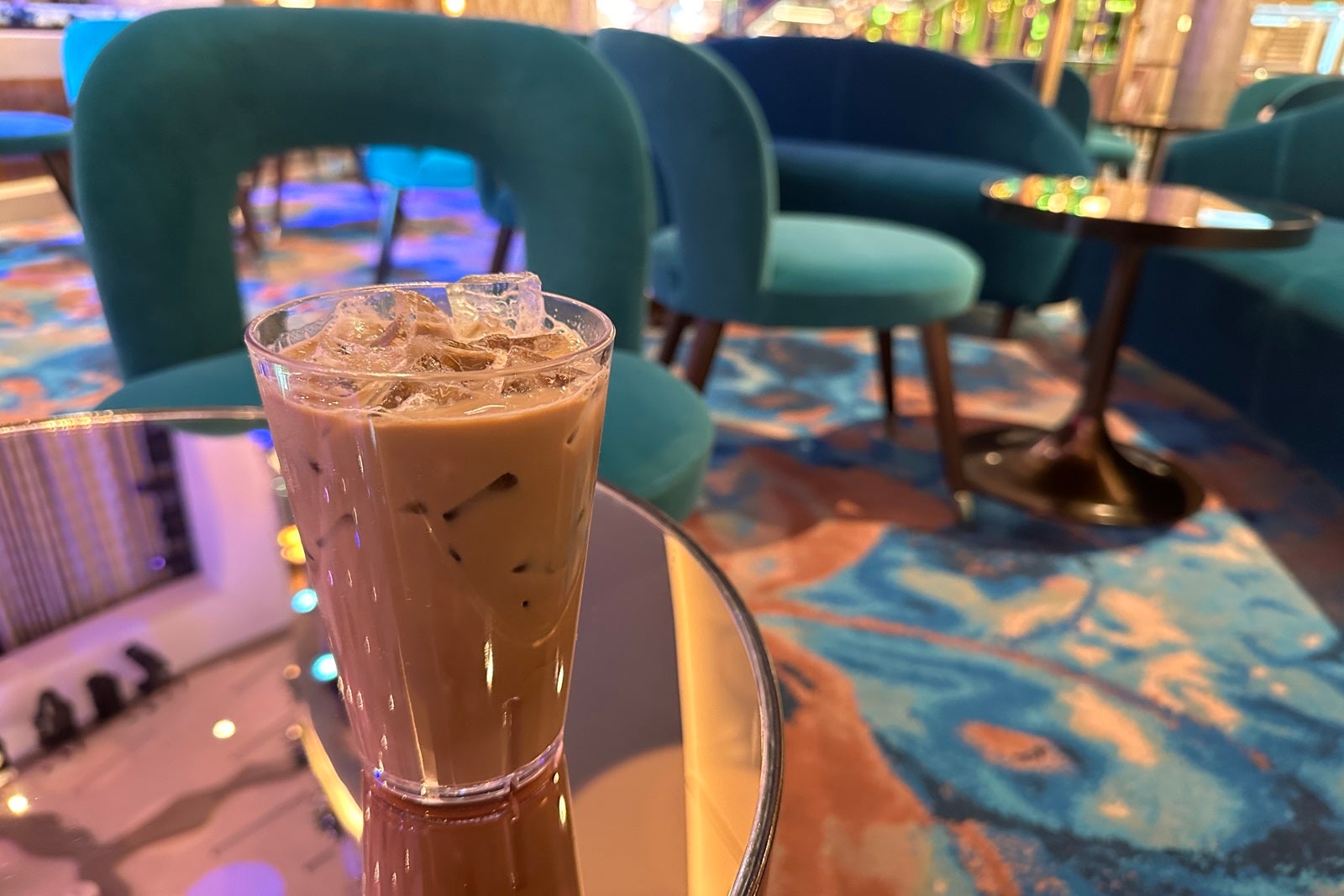 An iced coffee in a glass sitting on a table with teal chairs in the background