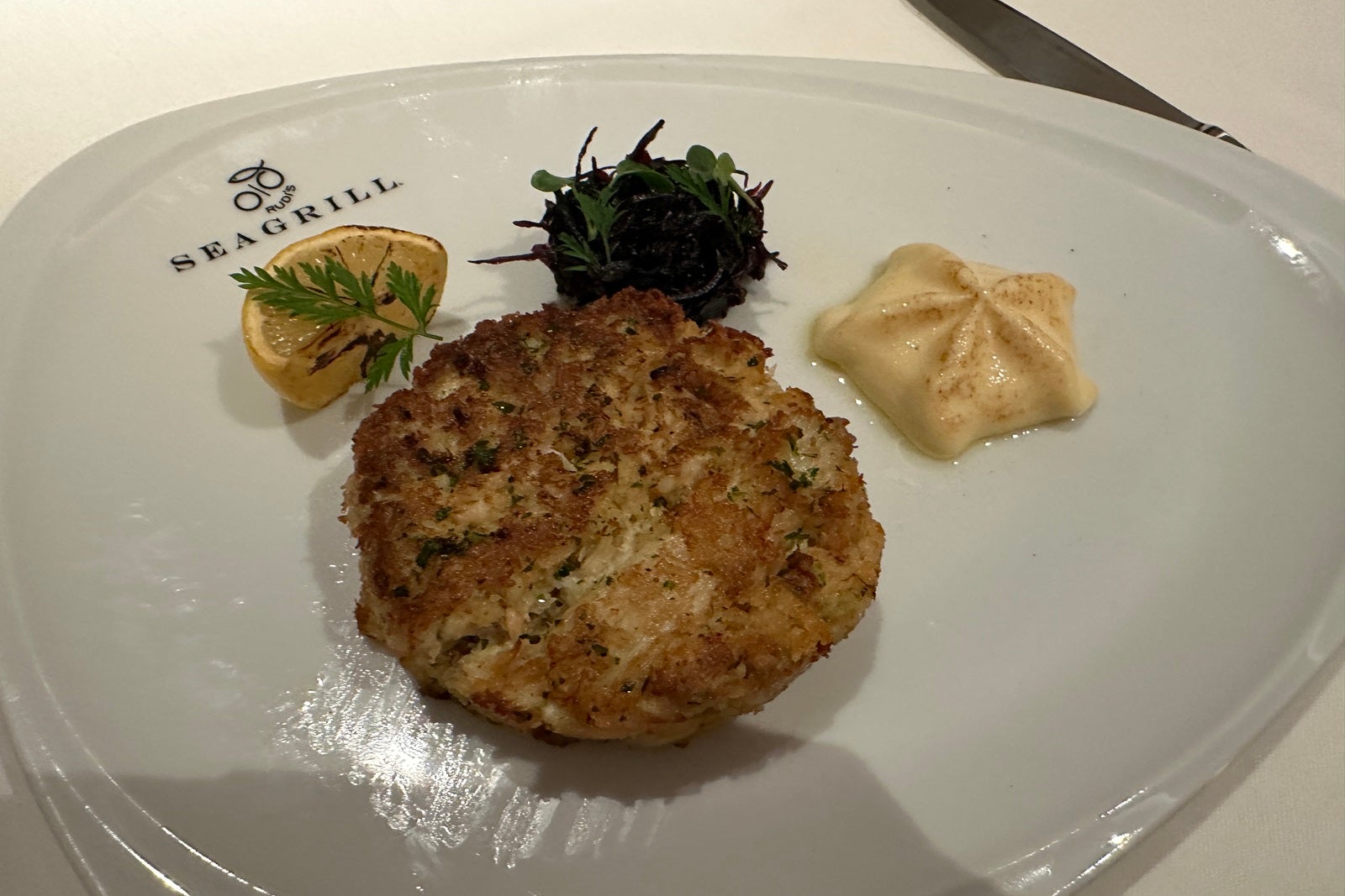 A crab cake on a white plate with side sauces and garnishes