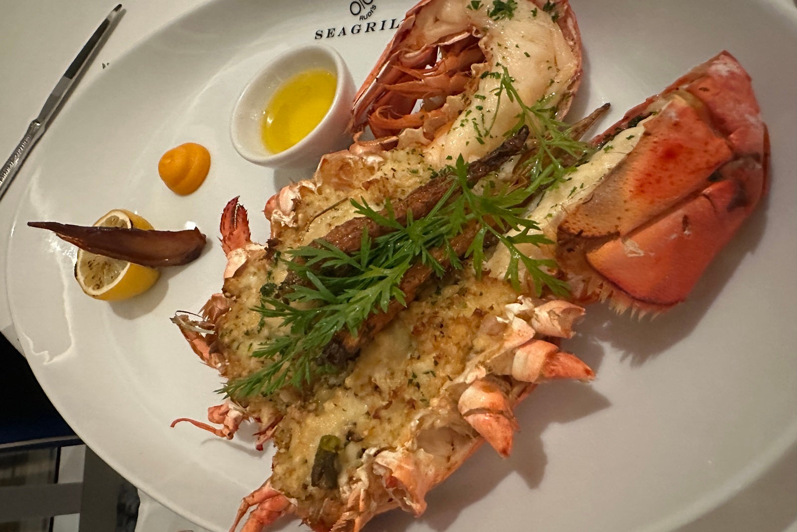 A lobster tail stuffed with crab and topped with herbs on a white plate with a side of butter
