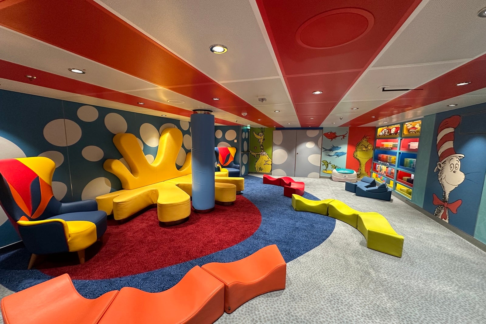 A colorful room with bright red, blue, orange and yellow furniture, murals of Dr. Seuss characters and bookshelves