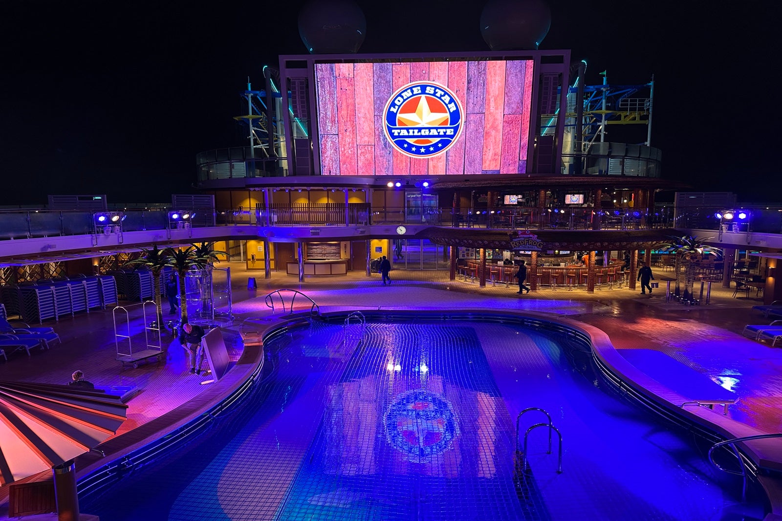 A cruise ship pool at night with a movie screen above it