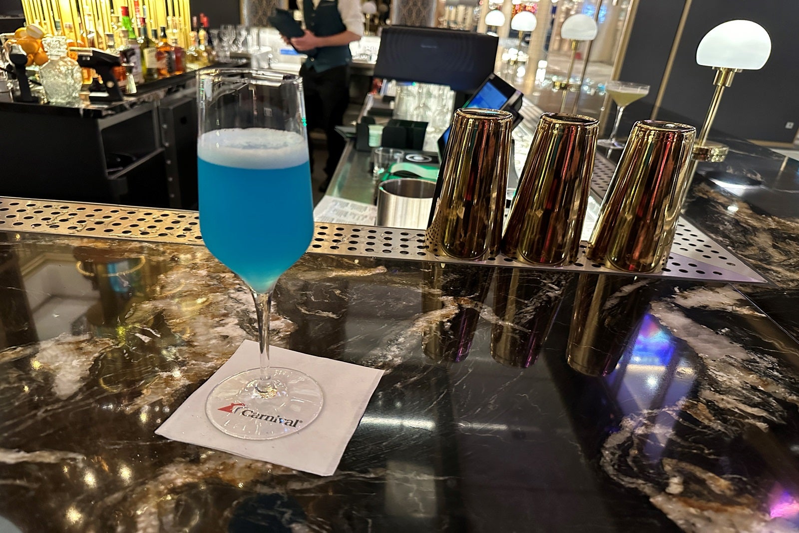 A tall, stemmed drink glass with a blue cocktail set on a bar