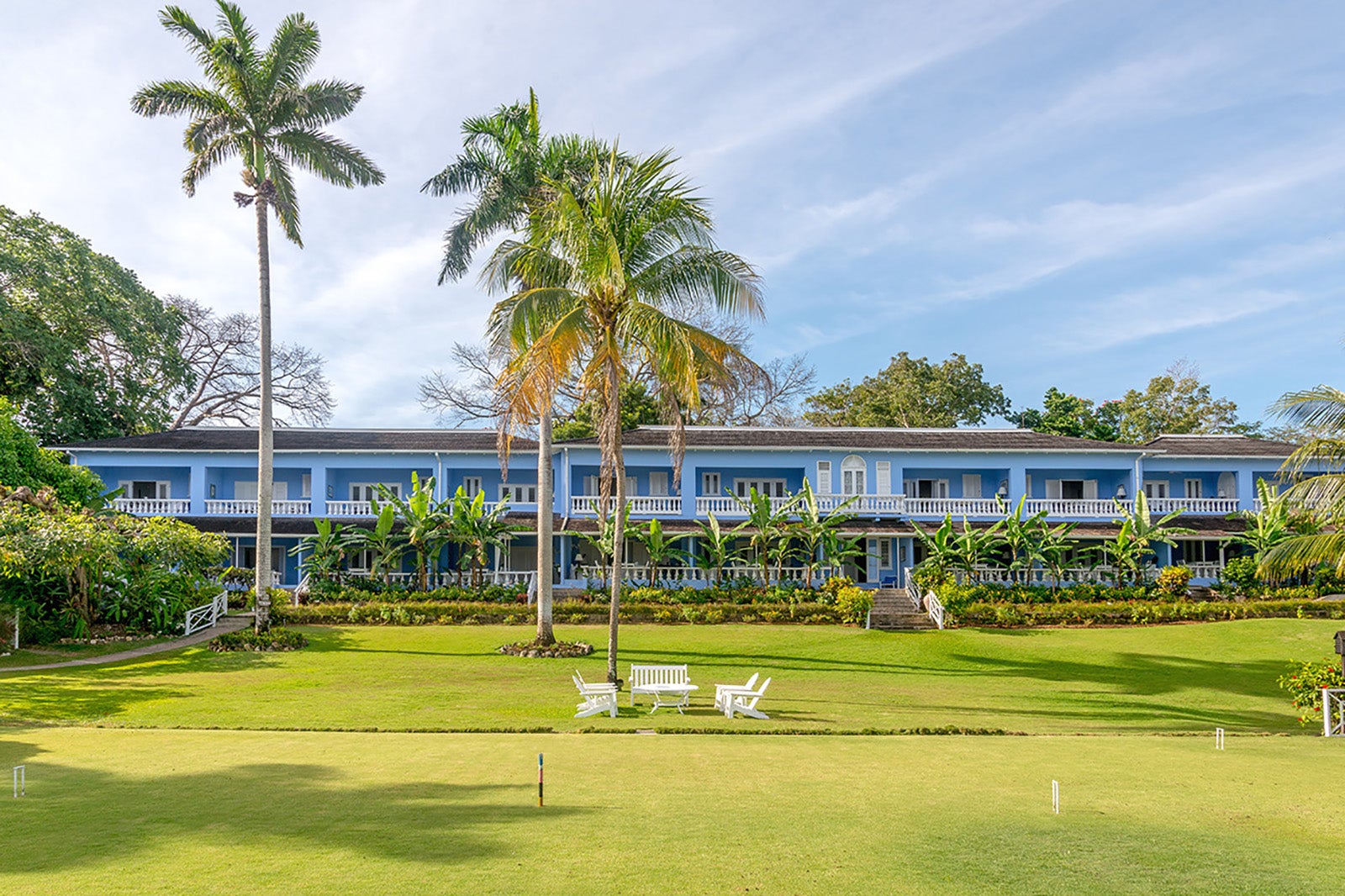 a blue two-story hotel with balconies surrounded by palm trees and a green lawn