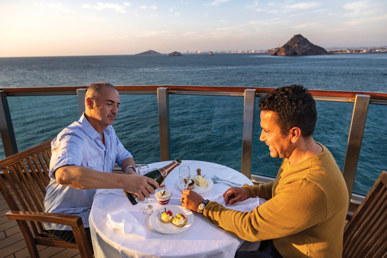 Two men enjoying Champagne during dinner on their balcony on a Princess cruise.