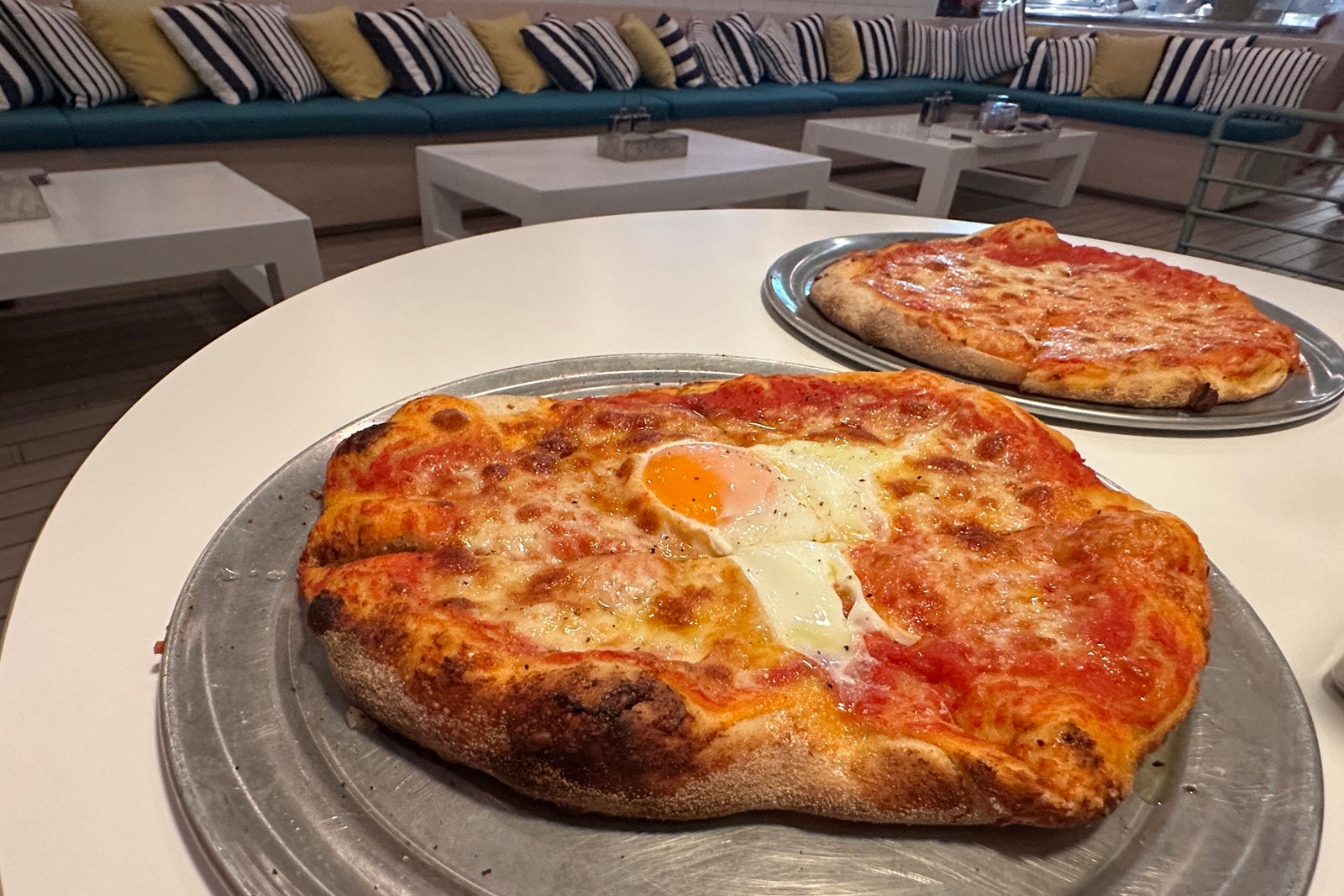 Two pizzas on metal trays sitting on a table