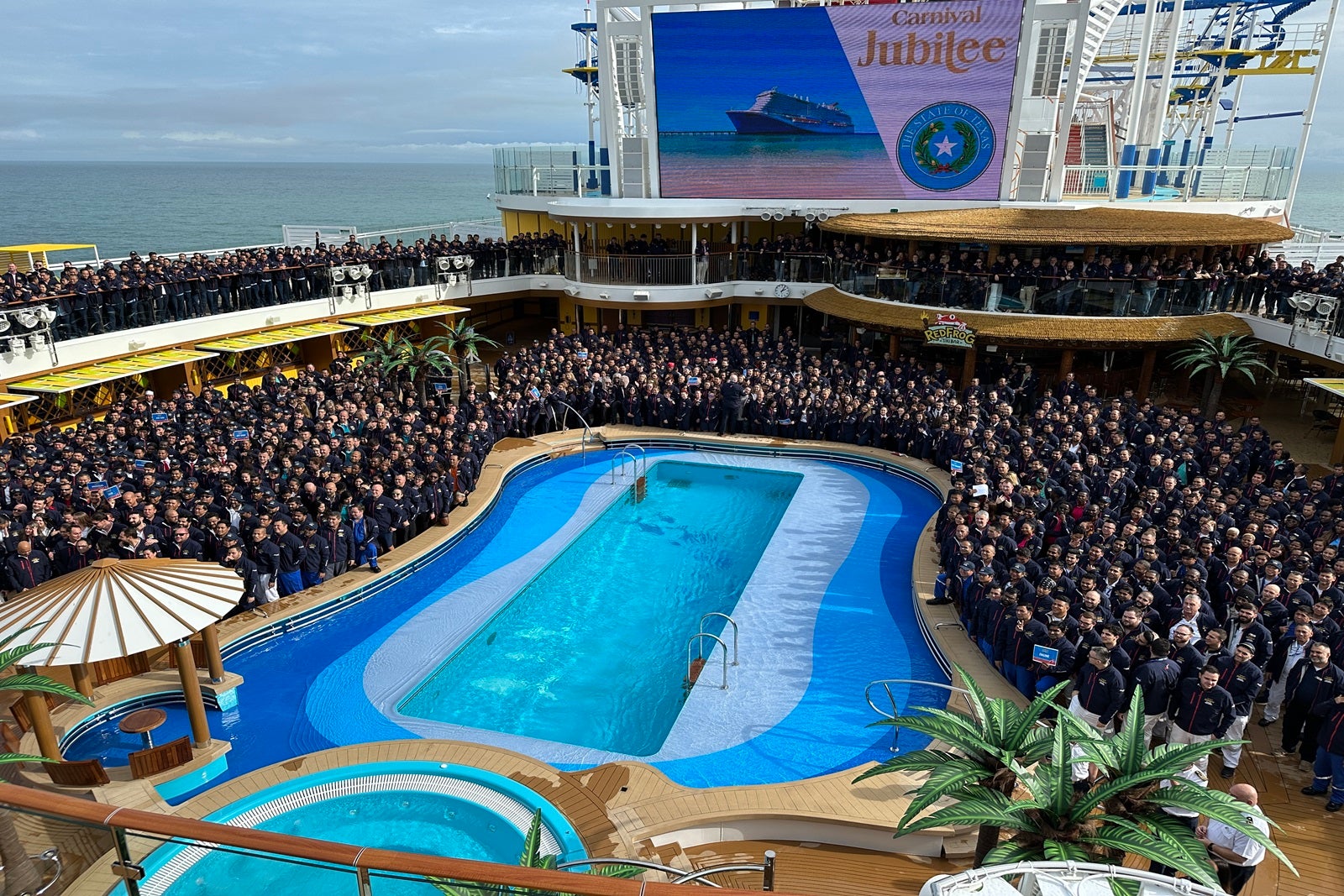 A large group of cruise line employees gathered around a pool on a cruise ship