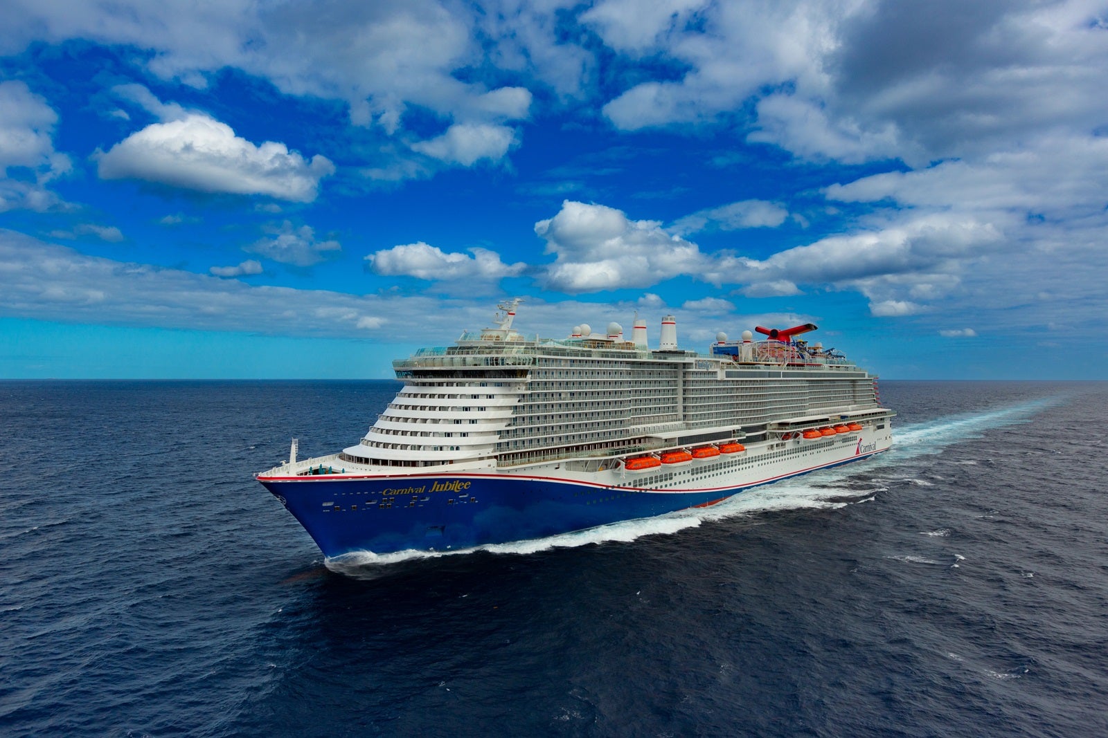 A cruise ship with a blue hull sailing on blue water in front of a blue sky with white clouds