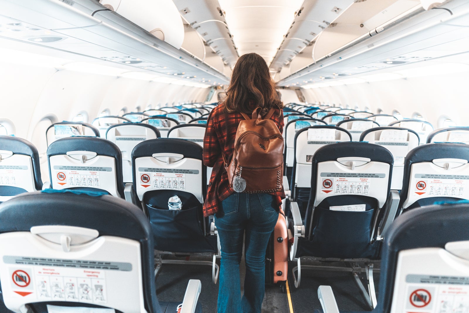 Woman with backpack walking down airplane aisle