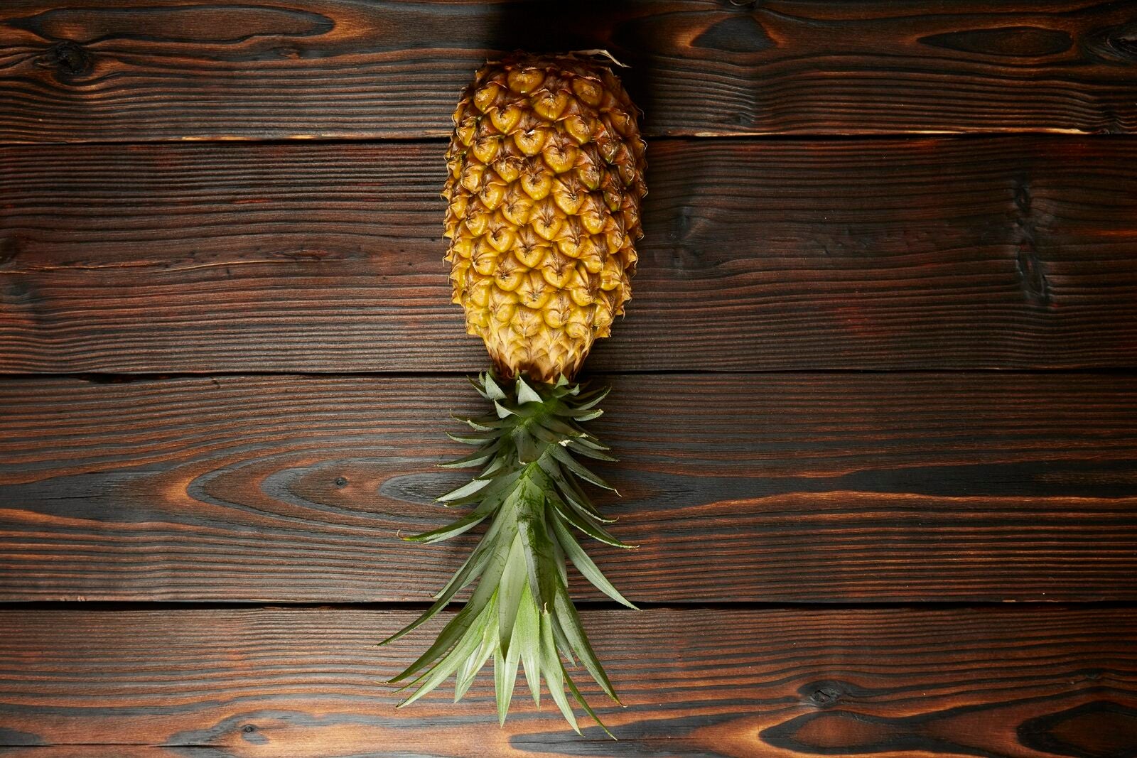 A pineapple lying on a wooden table, upside-down