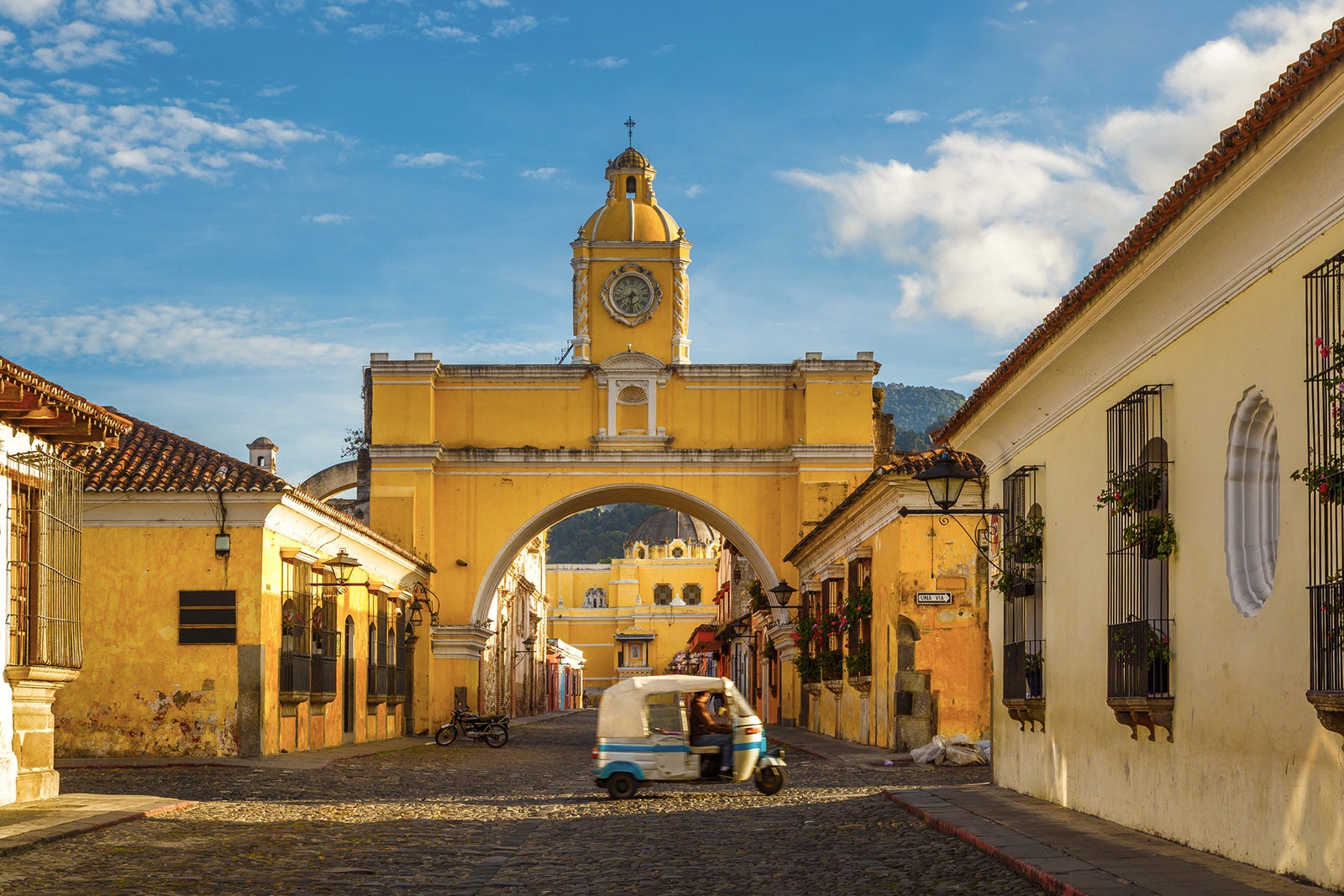 a tuk-tuk taxi passes in front of The Arch of Santa Catalina in Antigua, Guatemala.