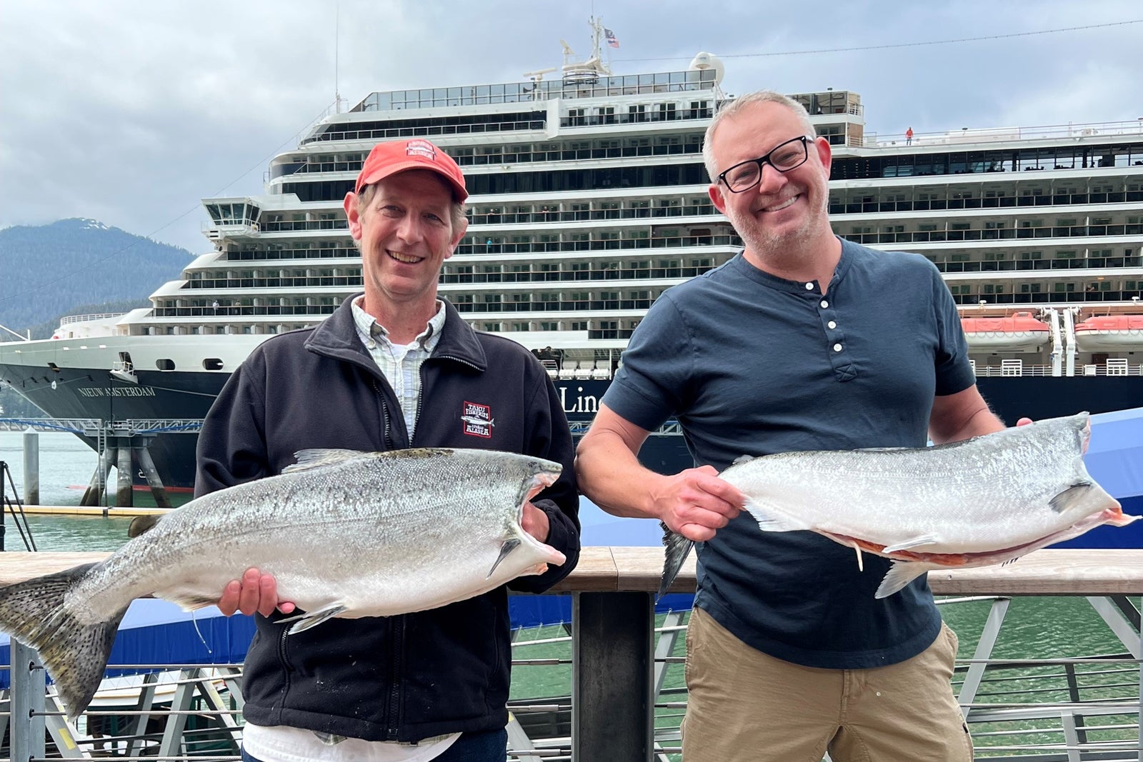 Two men holding fish in front of Holland America cruise ship