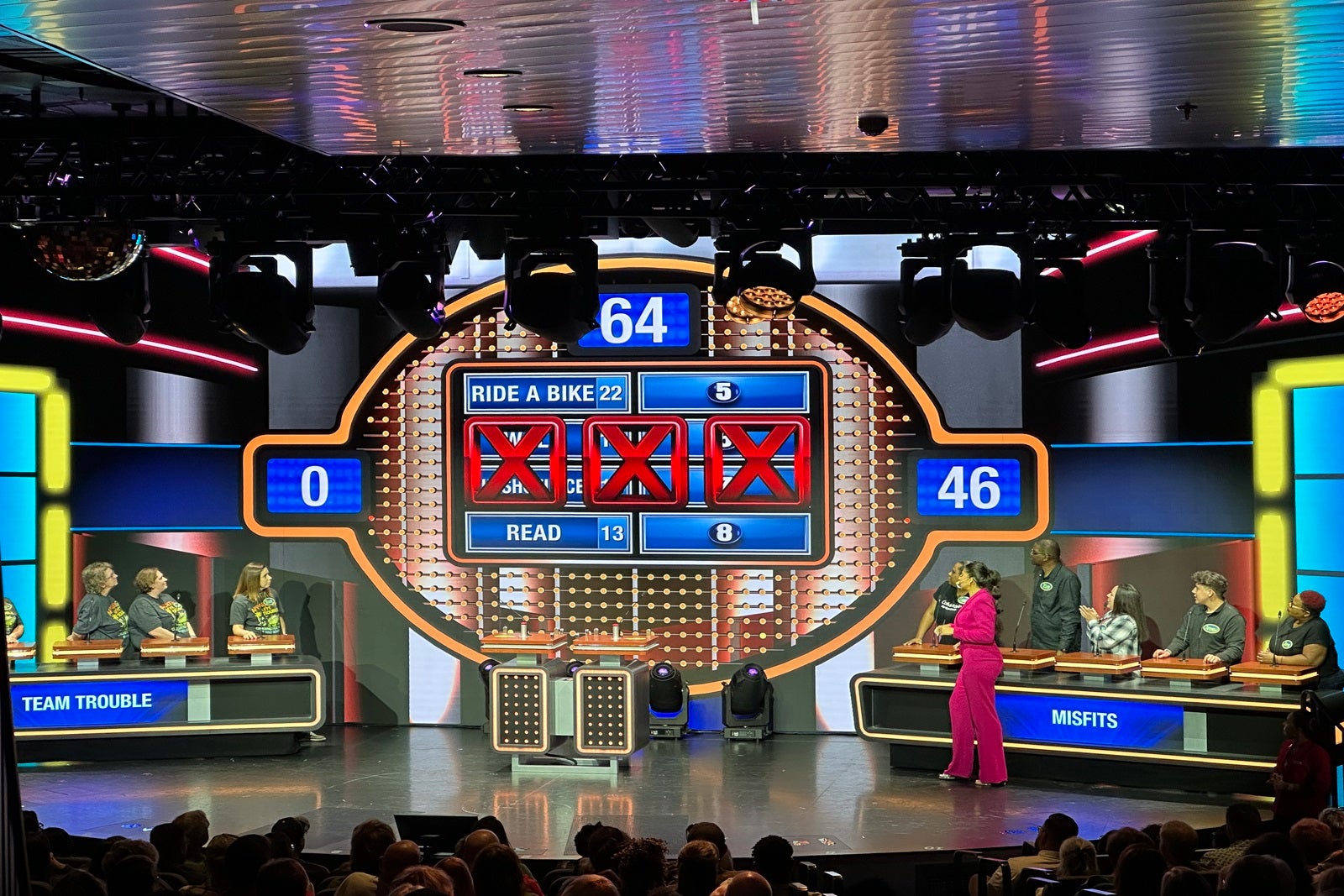Two teams playing Family Feud on a cruise ship stage in front of a giant LED screen