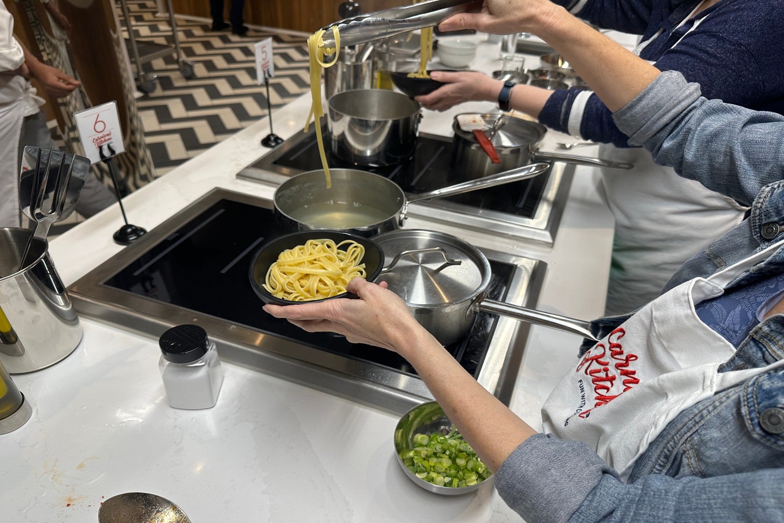 A pair of hands preparing a pasta dish over a cooktop