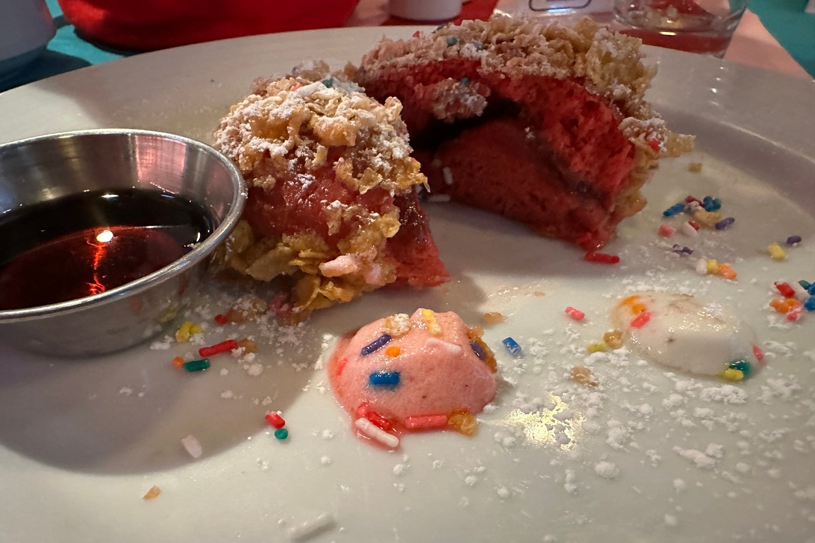 A white plate with a round piece of red velvet French toast with sprinkles
