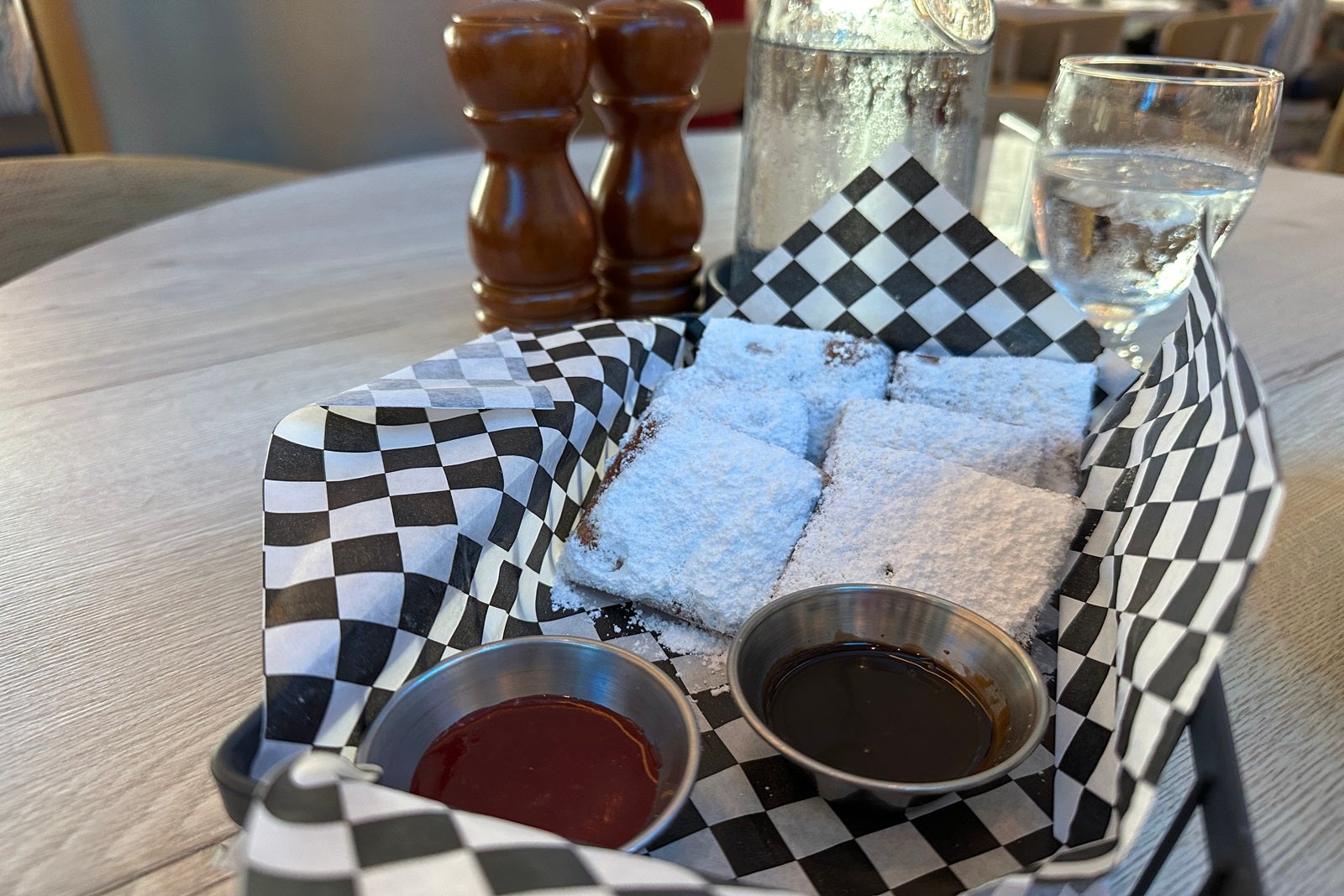 A basket of sugared beignets on black and white checkered paper