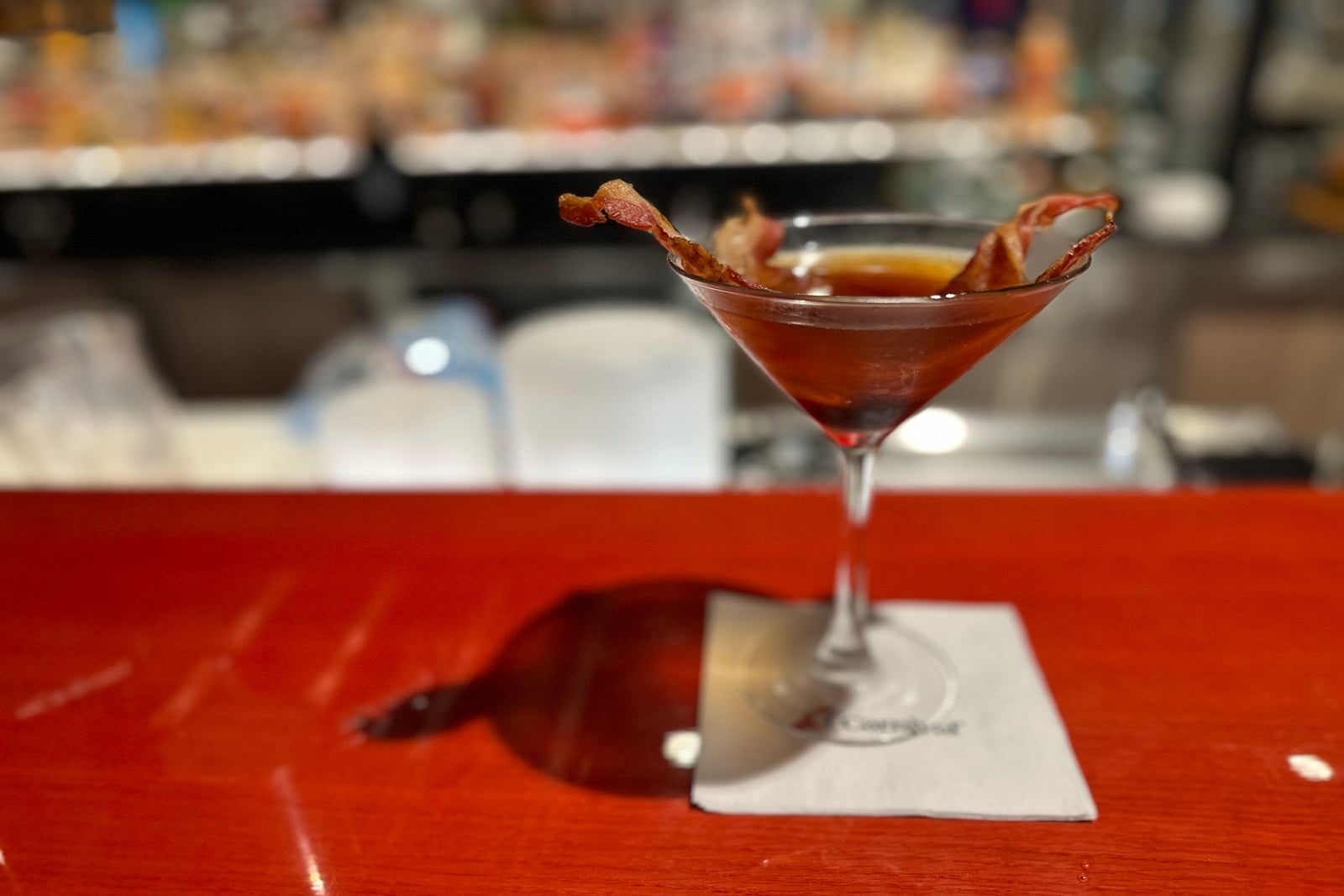 A bacon Manhattan standing on a red bar top