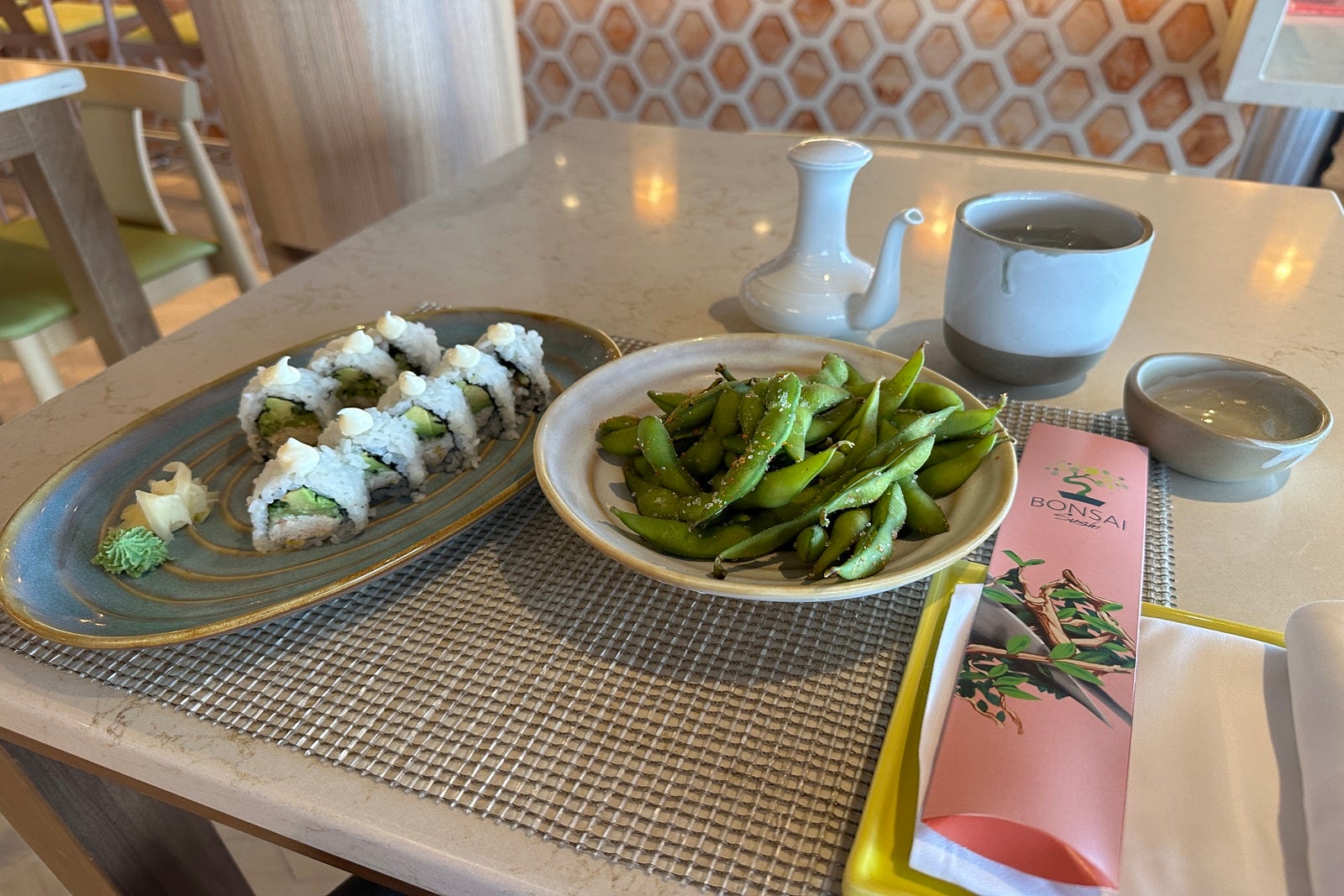 A California roll and edamame on plates on a table with chopsticks