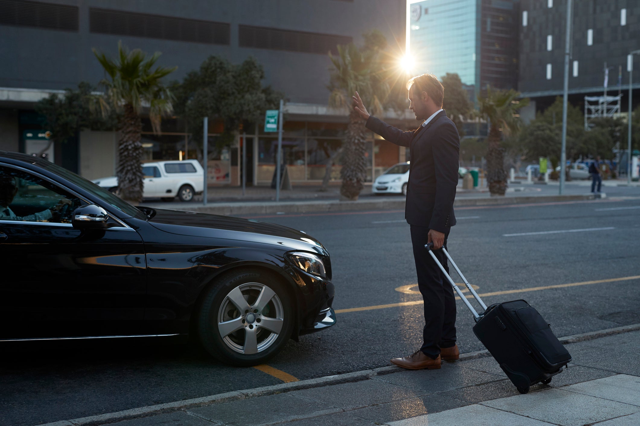 Businessman with rolling suitcase hailing a cab