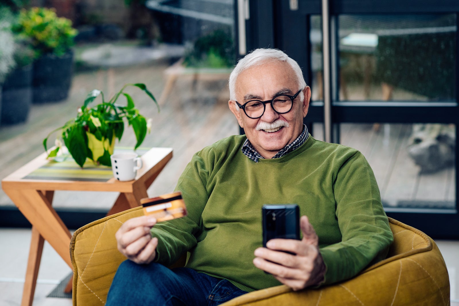 elderly man sitting in a chair holding a credit card and phone