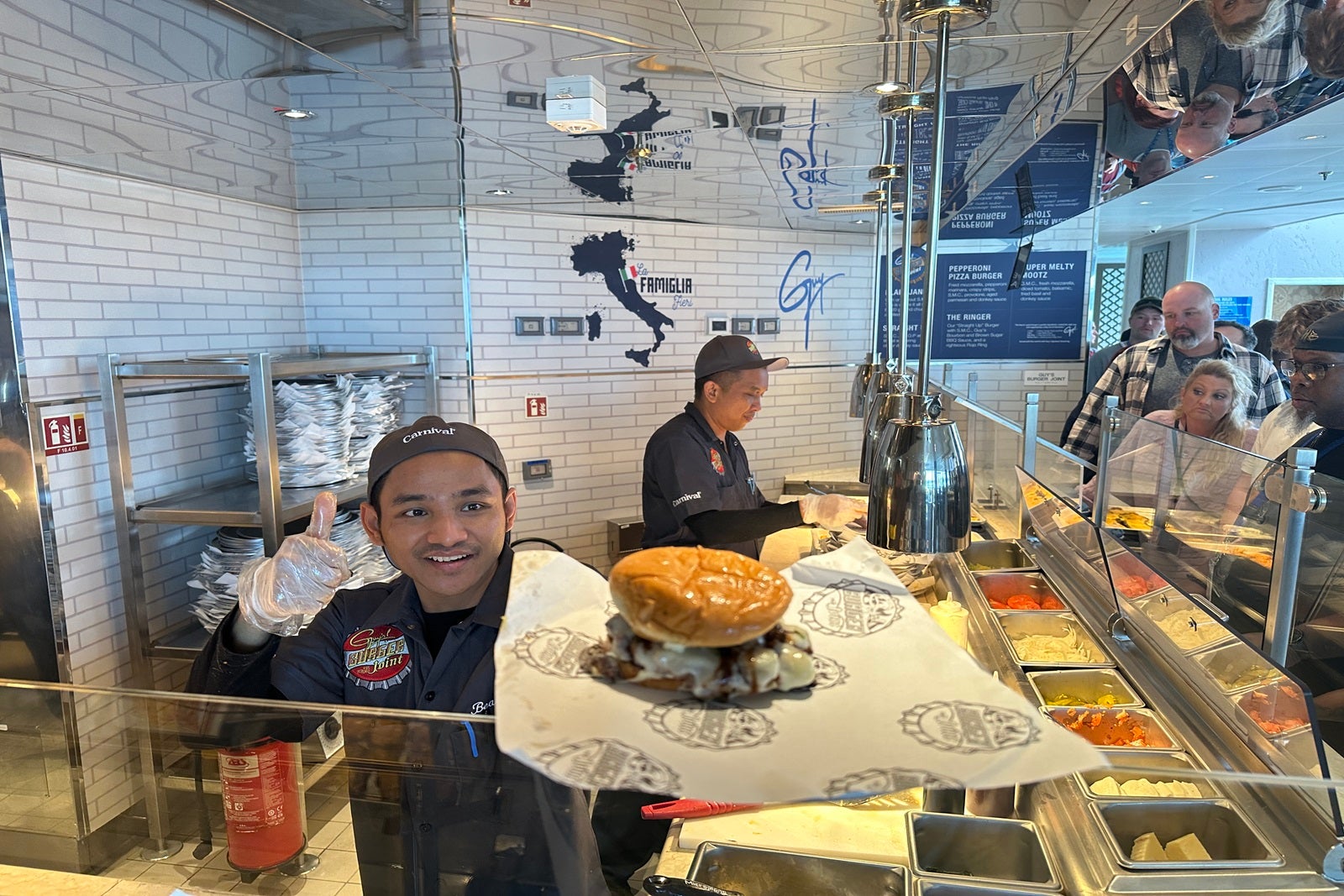 A cruise ship crew member hands a cheeseburger over the counter to a customer