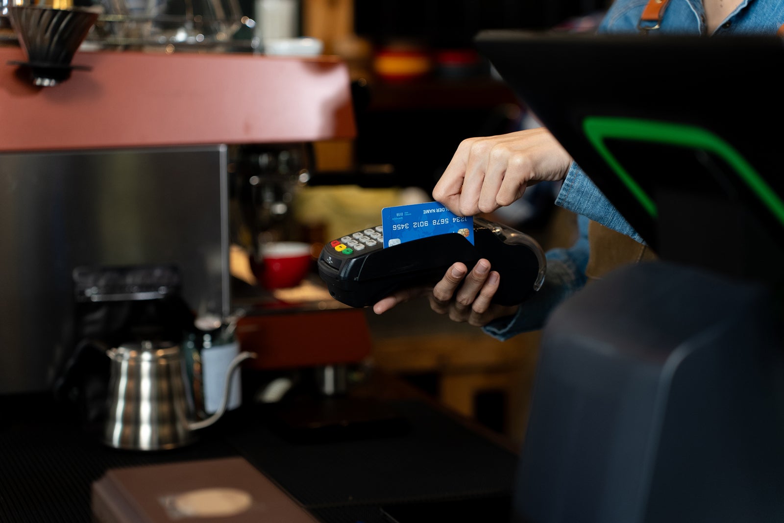 person sliding a credit card through a reader in a coffee shop 